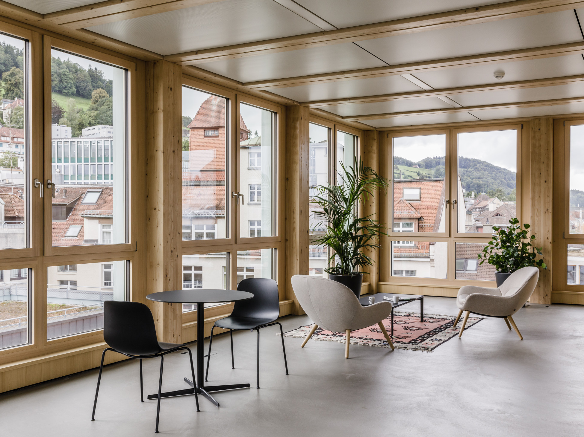 Medisuisse Frongarten, St. Gallen Medisuisse Frongarten, St. Gallen - Zimmer von innen, mit Fensterfront aus Holz, zwei Tische mit Stühlen und zwei Pflanzen
